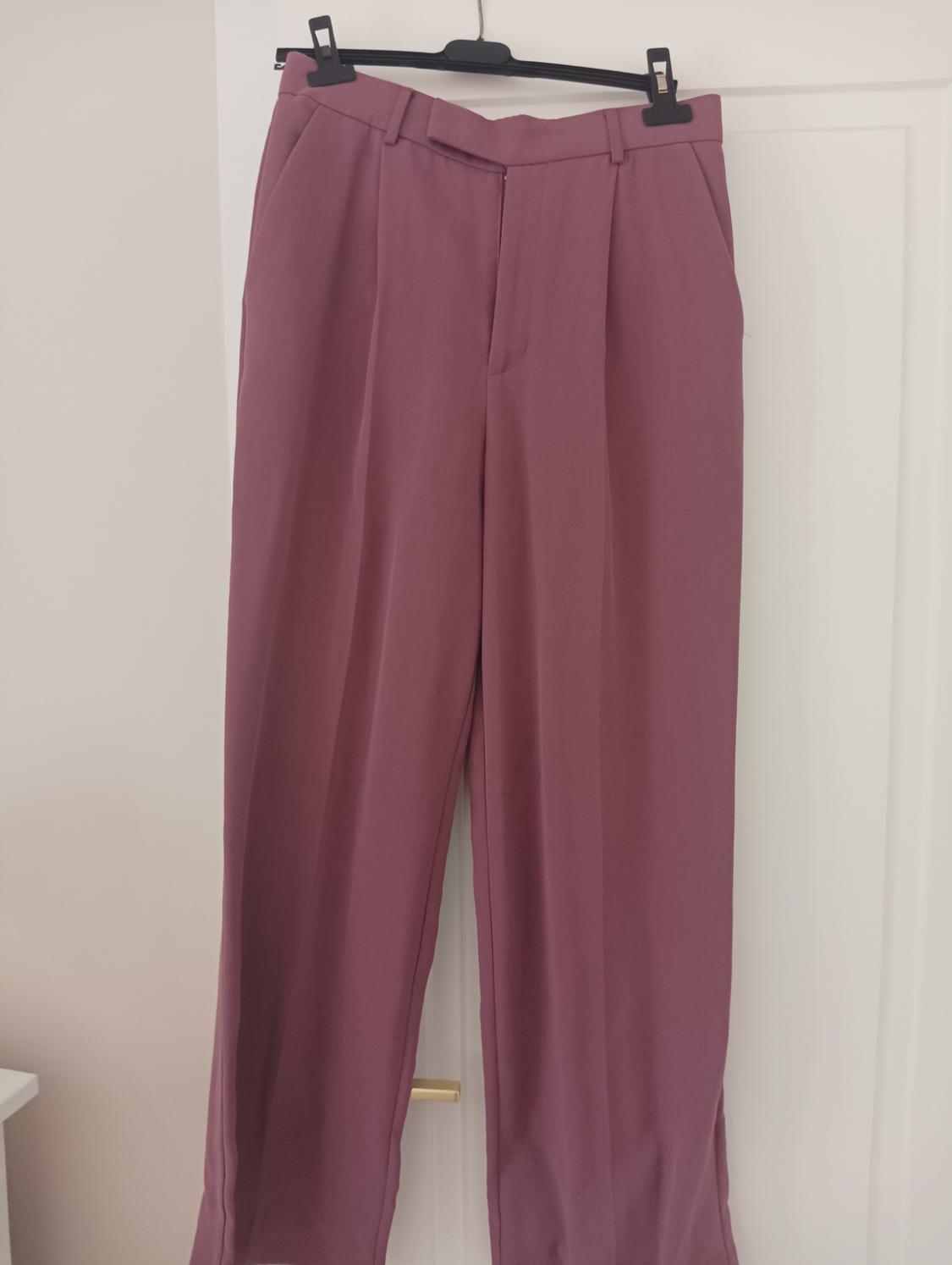 Dark pink dress trousers hung on a black hanger over a white door.