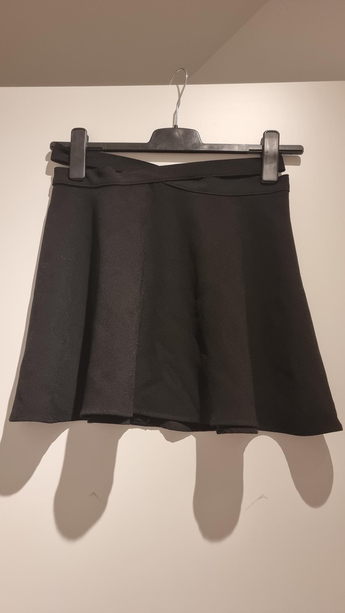 Short black skirt hanging on a black hanger against a white background, illuminated by a soft light that casts shadows.