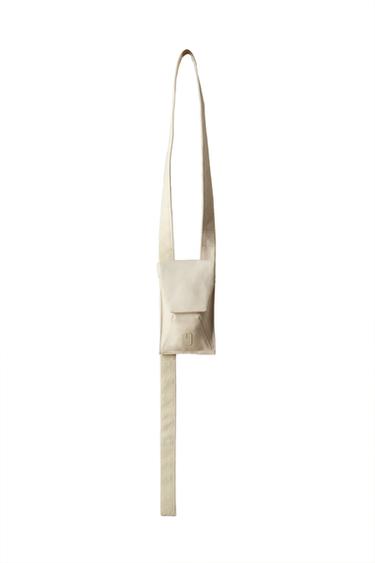 Front view of a beige handbag with flap and long strap.