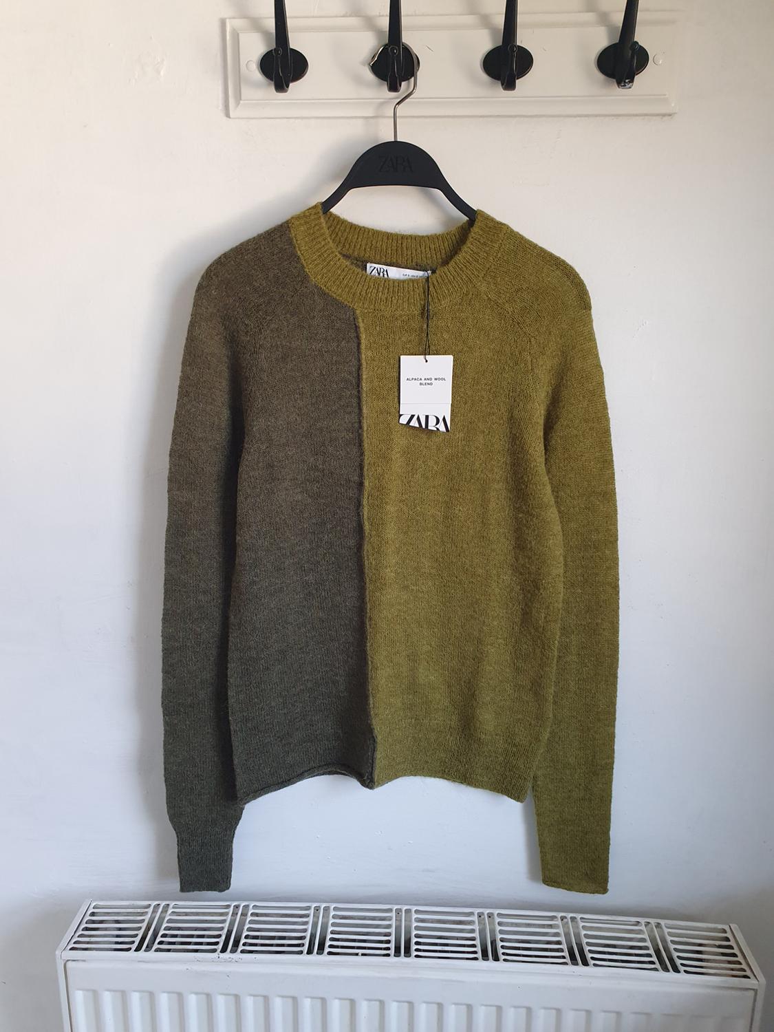 A two-tone jumper hanging on a black Zara hanger, with a label that reads "ALPACA AND WOOL BLEND", against a white background.