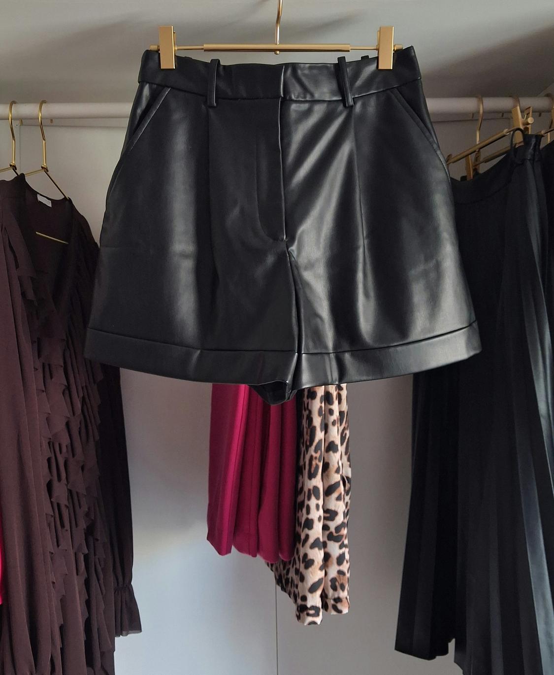 Black shorts hanging on a gold clothes rail, surrounded by brown, fuchsia, and leopard print garments.