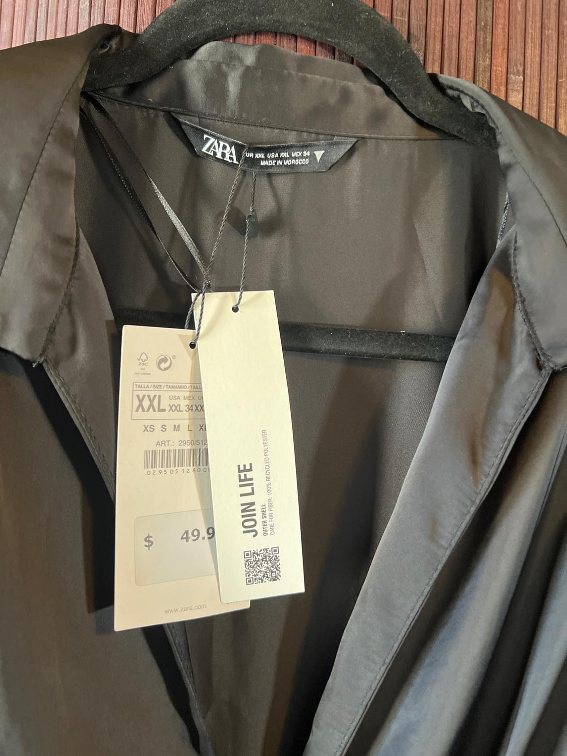 Black Zara shirt on hanger with "JOIN LIFE" tag, size XXL, price $49.99, made in Morocco. Brown wooden background.