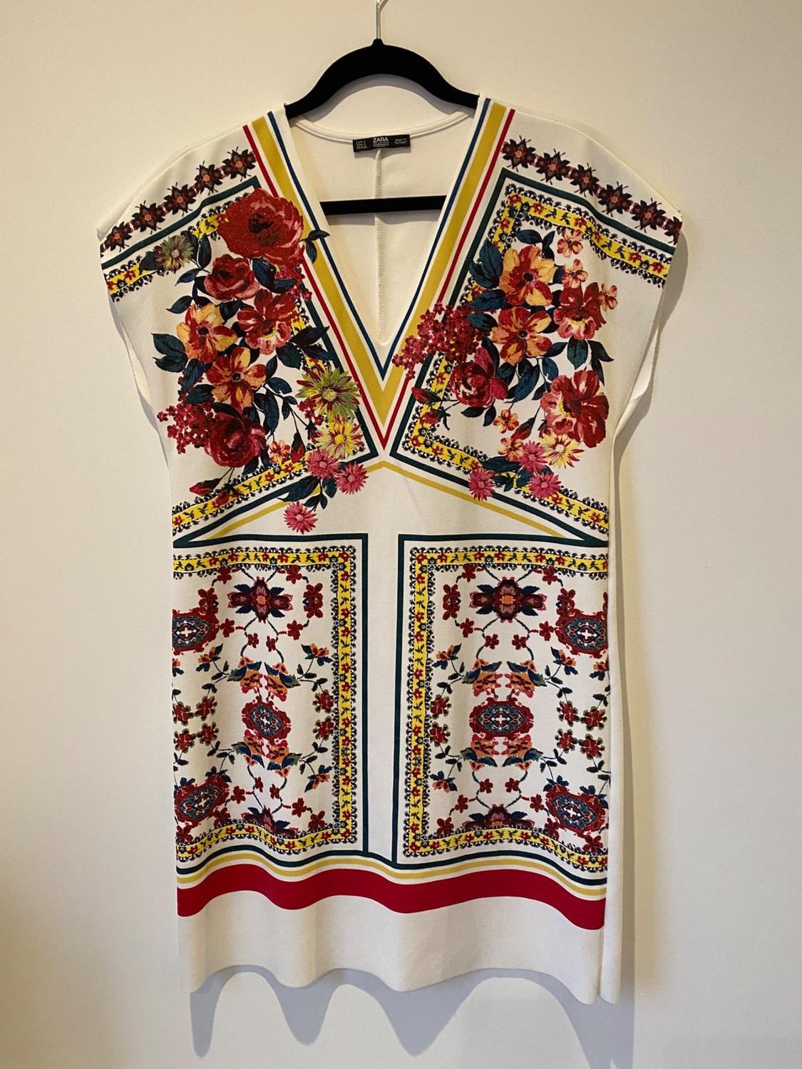 Front view of white dress with red and yellow floral print, V-neck and vibrant colour details.