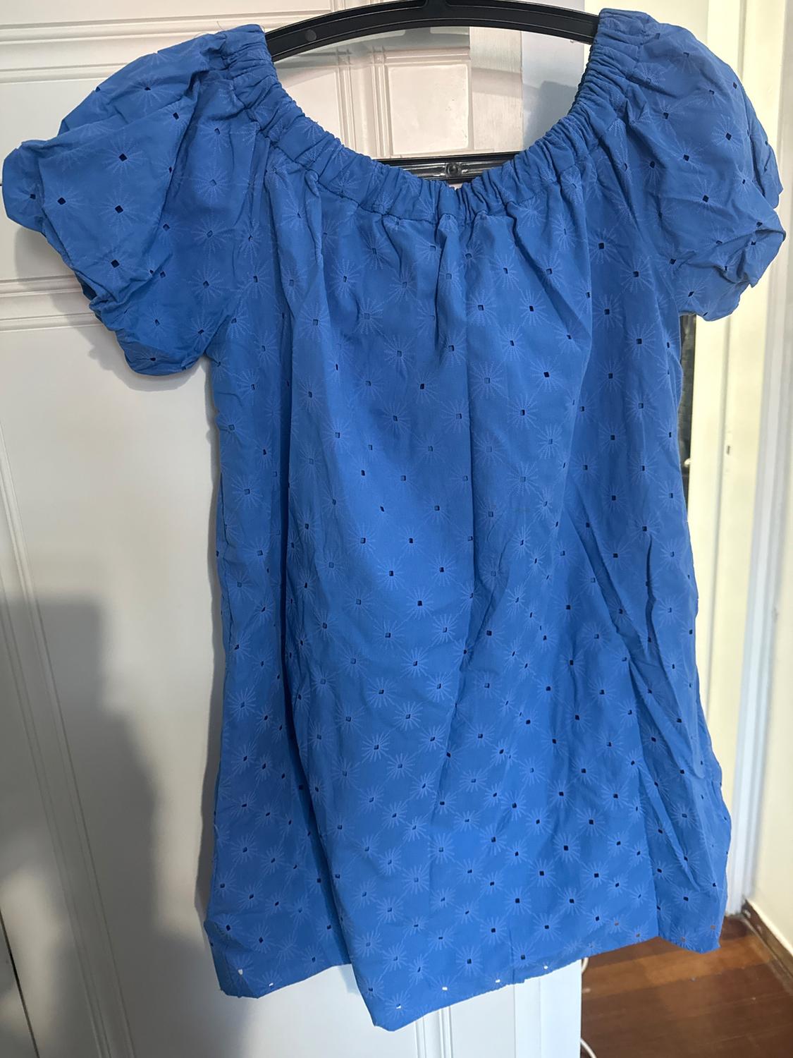 Blue dress with puff sleeves and a small hole design, hanging on a hanger in front of a white door.
