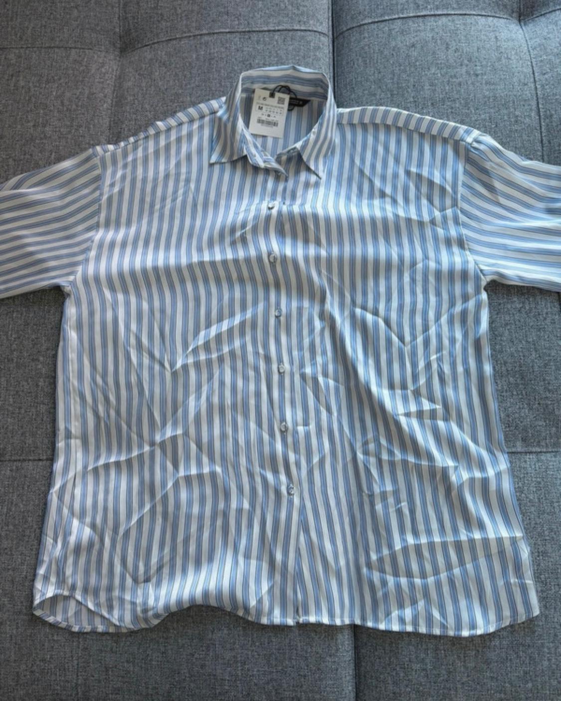 Blue and white vertical striped shirt with front buttons and label, laid out on a grey fabric surface.