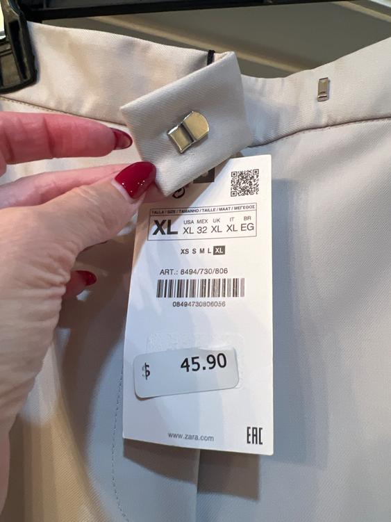 A clothing tag with a price of $45.90 and size XL, held by a hand with red painted nails, shows a visible barcode.