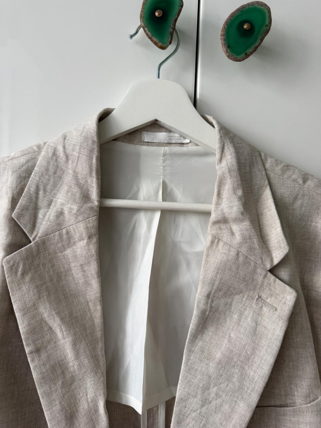 Beige jacket hanging on a white hanger, in front of a white wardrobe with green stone handles.