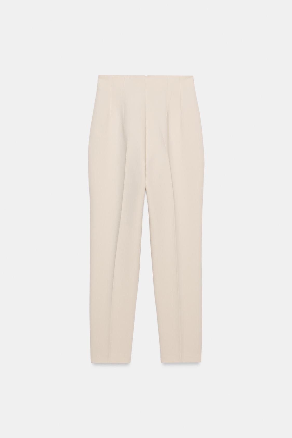 Sprednji pogled na hlače v naravni barvi, z visokim pasom, z izrazitimi šivi in sprednjimi žepi na robu. Sprednje zapenjanje z zadrgo.