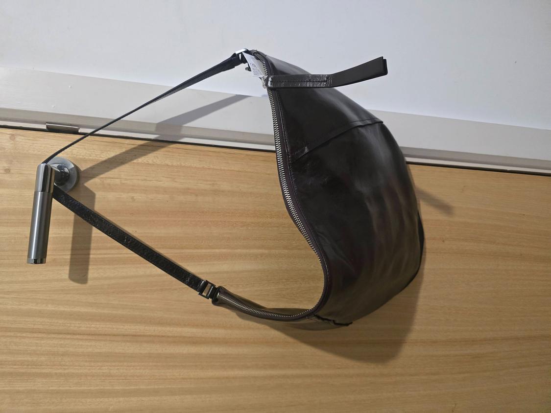 Black handbag with a zip and long strap, hanging from the metal handle of a wooden door. Relaxed, everyday setting.