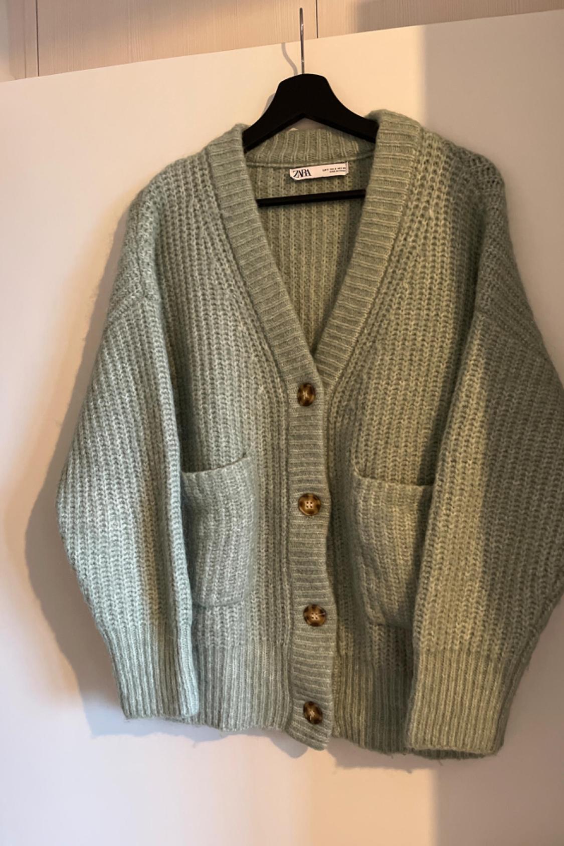 Front view of a green cardigan with brown buttons and front pockets.
