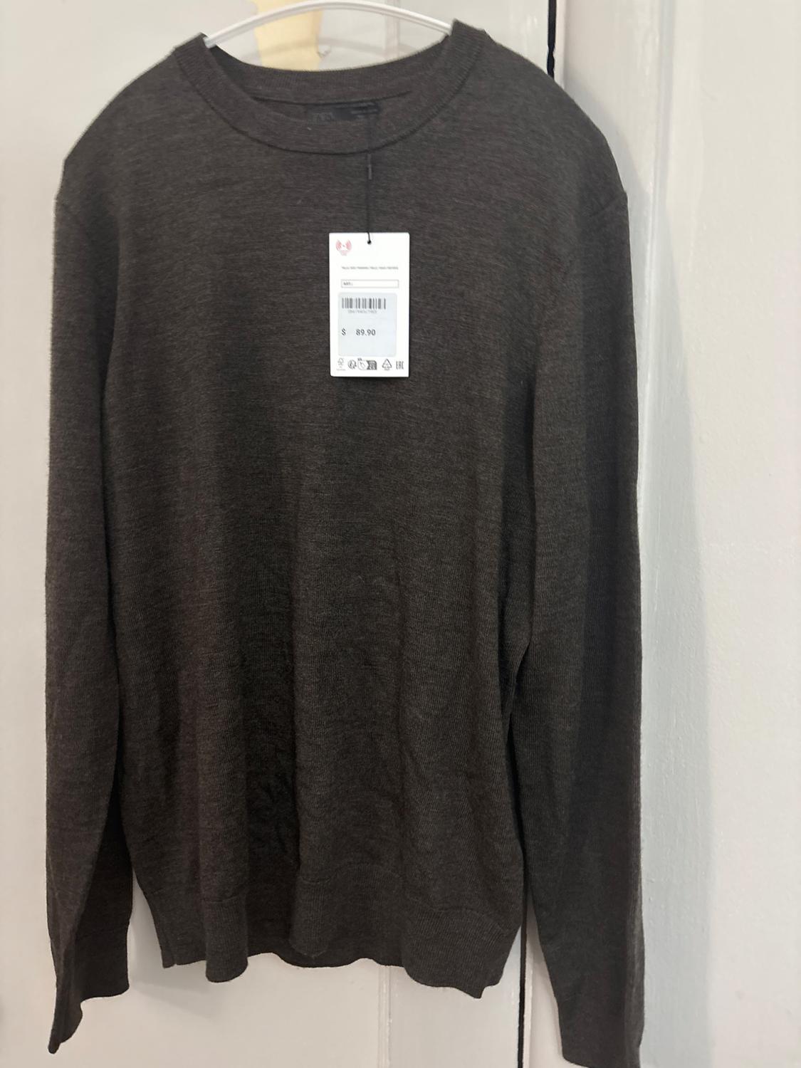 Dark grey knitted jumper with a round neck hanging on a white coat hanger. Includes a tag bearing the text $89.90.