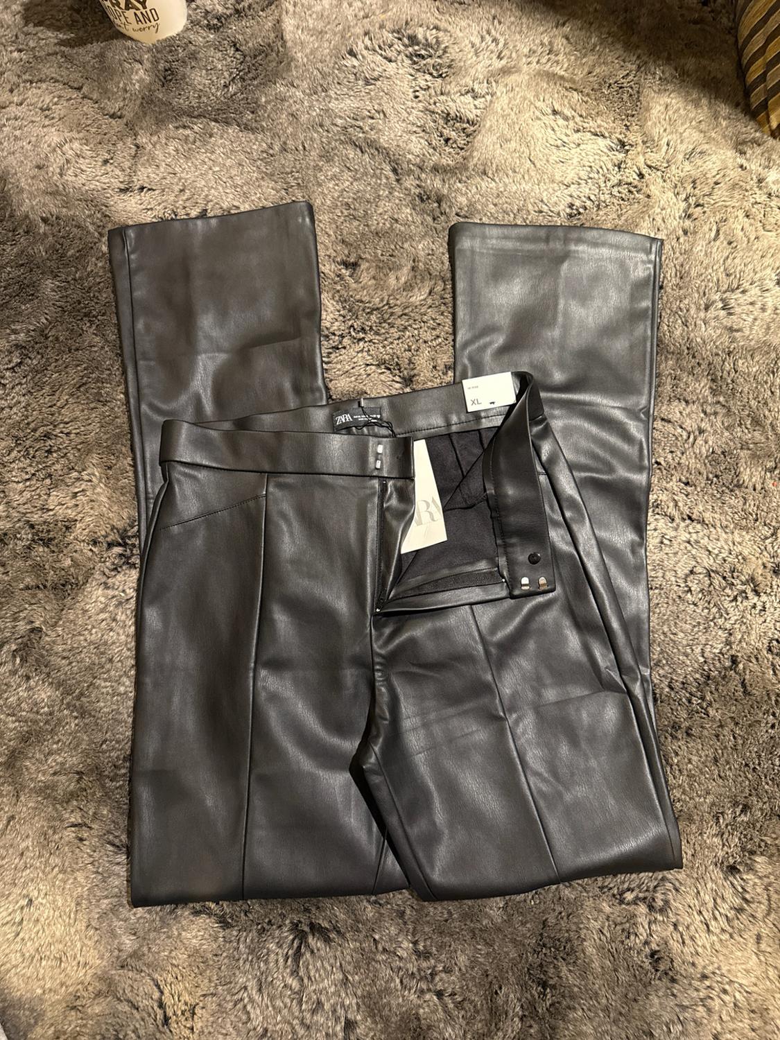 Unbuttoned black pants with ZARA and XL tags, spread out on a shaggy rug.