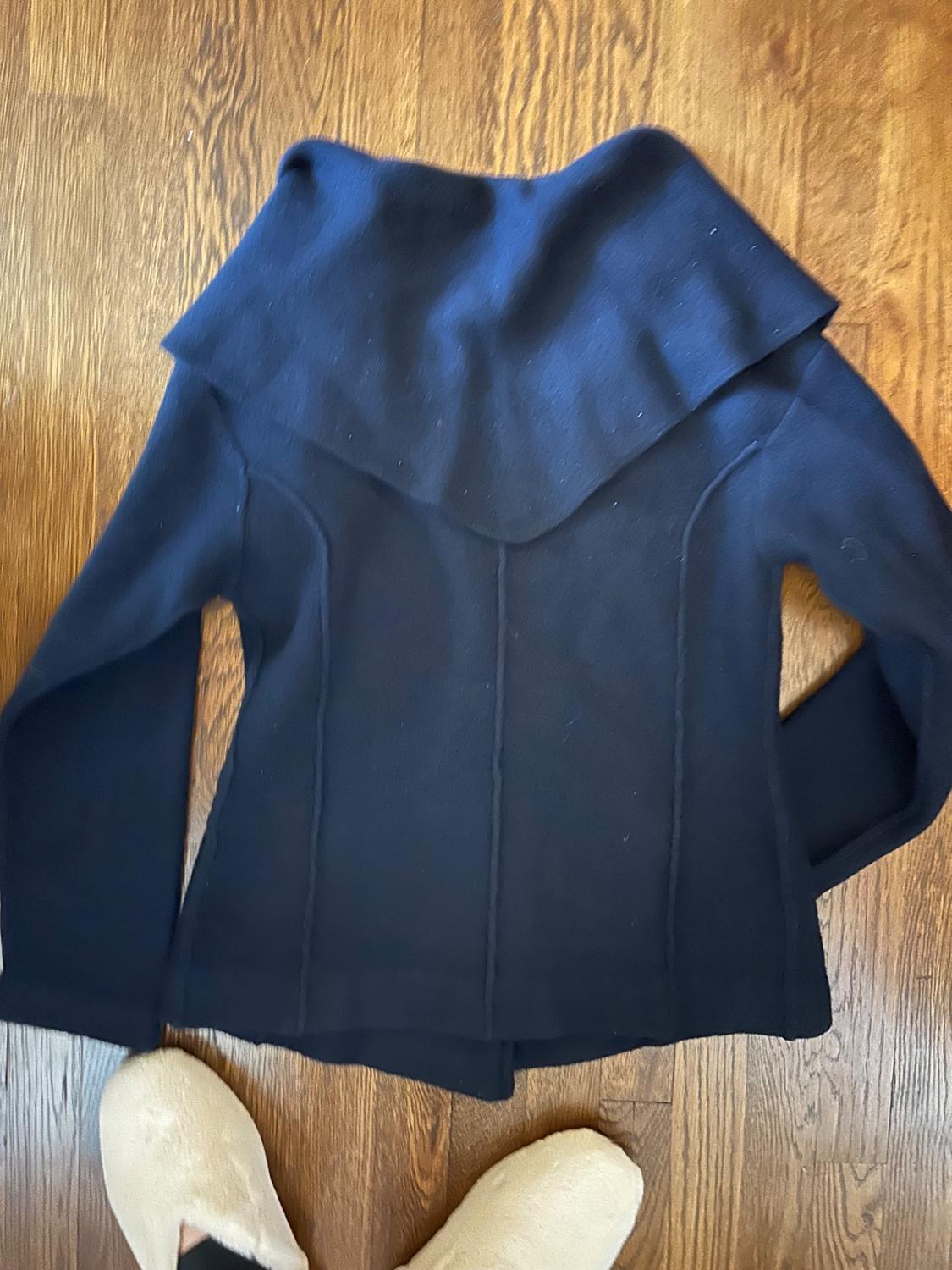 Black wool jacket with a wide collar on a wooden floor. Bottom of beige slippers visible in the lower corner.