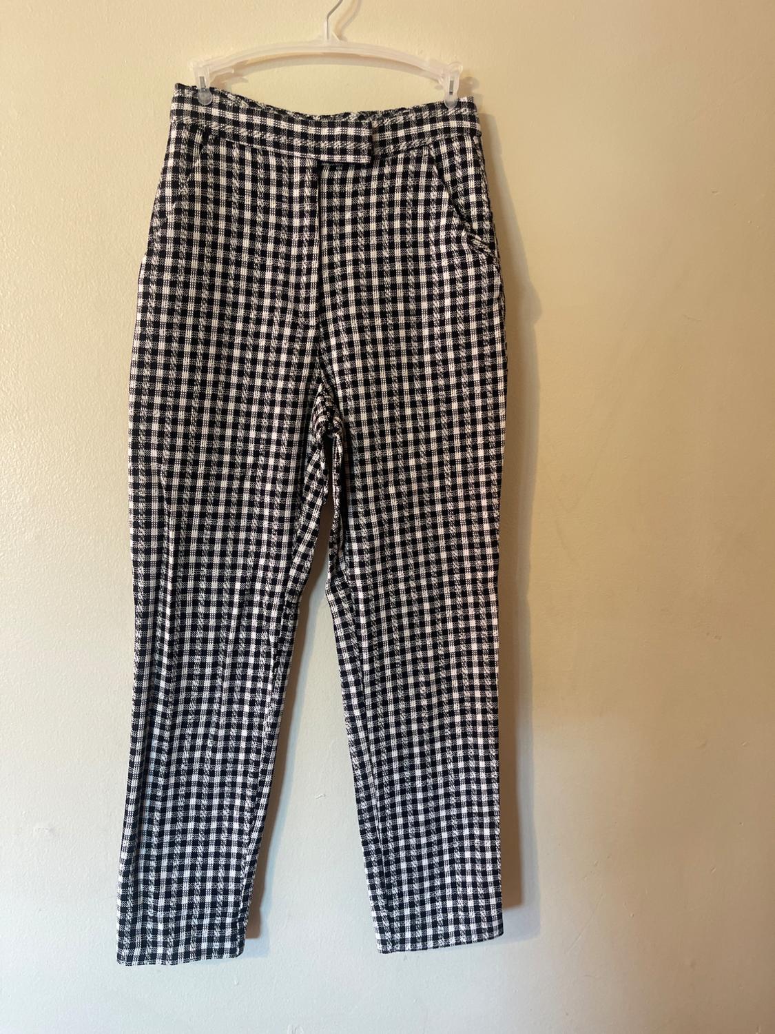 Black and white plaid pants hanging on a white hanger against a beige wall.