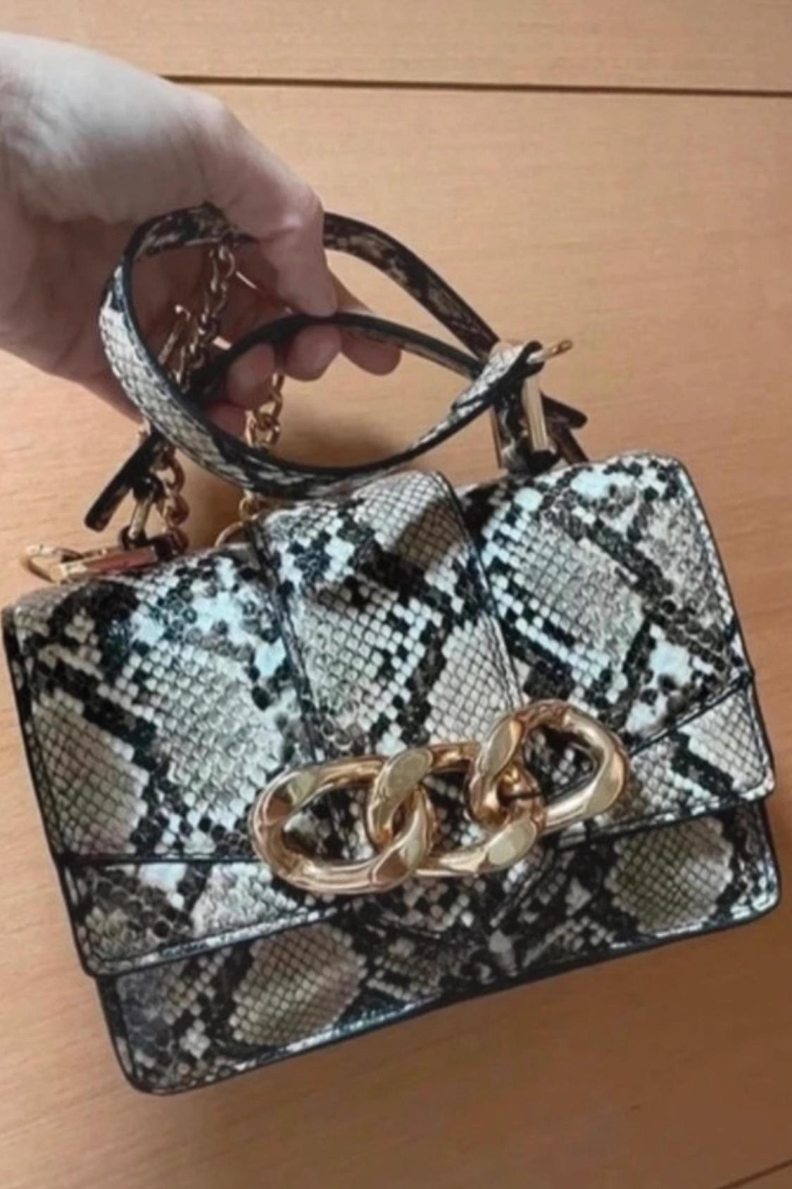 Close-up of handbag with snake print and gold chain.