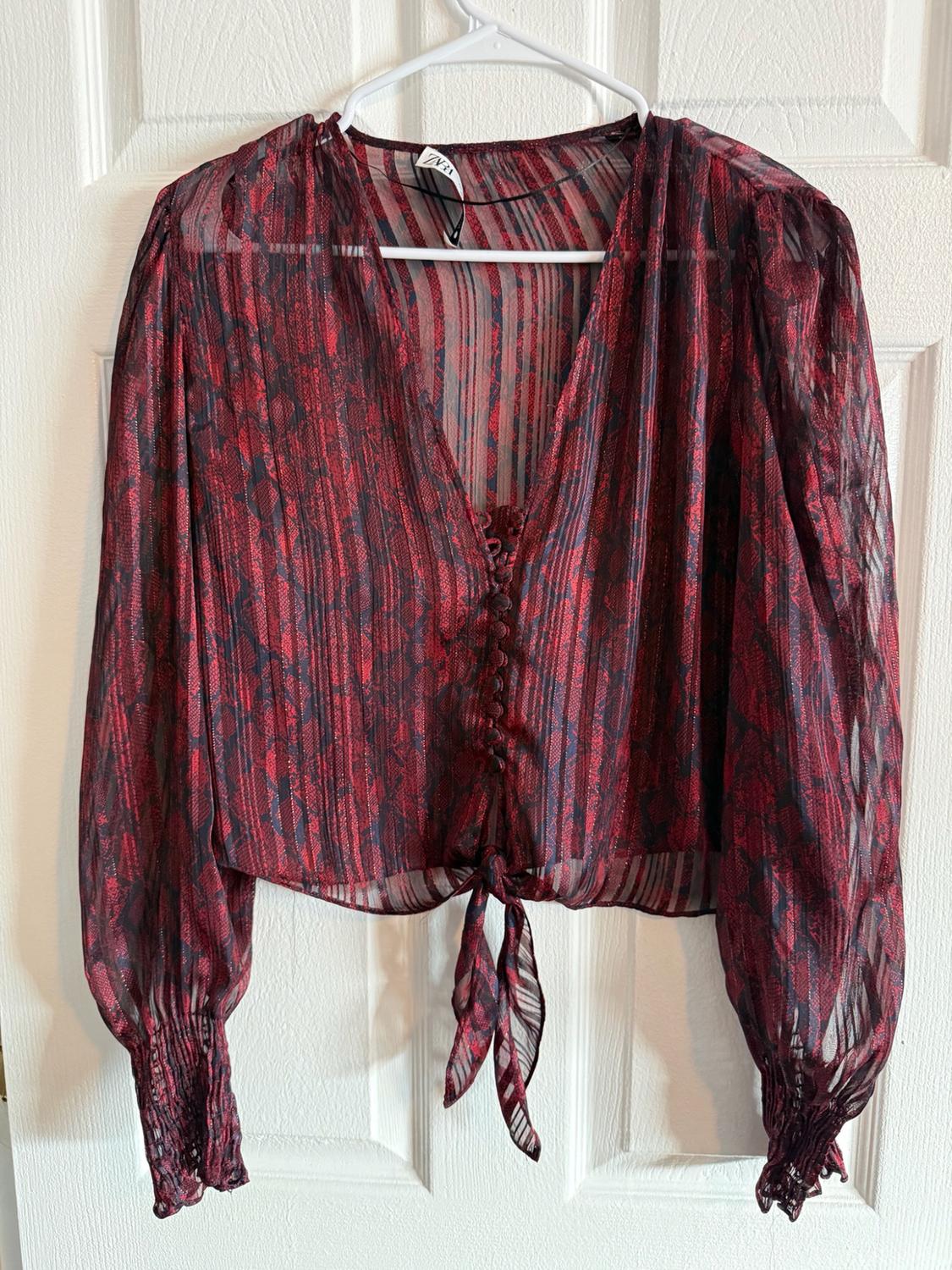 Long-sleeve Zara blouse, semi-sheer fabric with a red and black print, V-neck, front buttons, and a tie at the hem over a door.