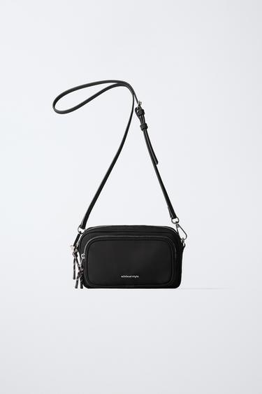 Frontansicht einer schwarzen Tasche mit verstellbarem Riemen, Fronttasche mit Reißverschluss und sichtbarem Text "minimal style".