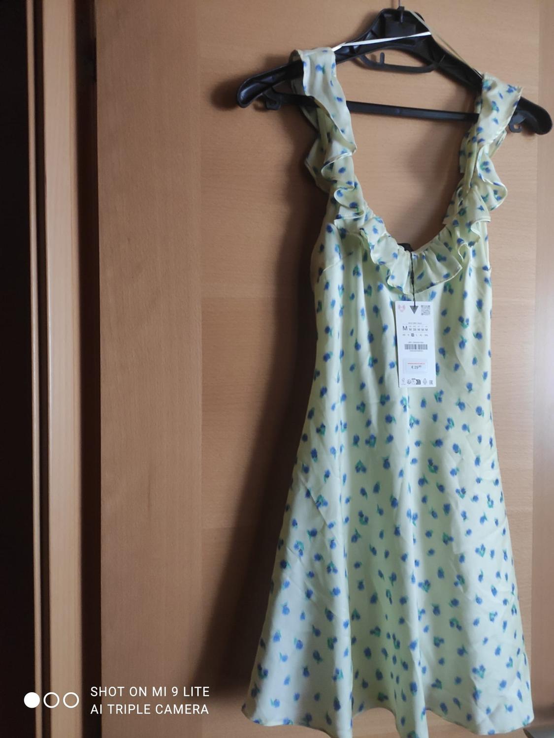 Yellow dress with blue flowers and frills, hanging on a door. Text: SHOT ON MI 9 LITE AI TRIPLE CAMERA.