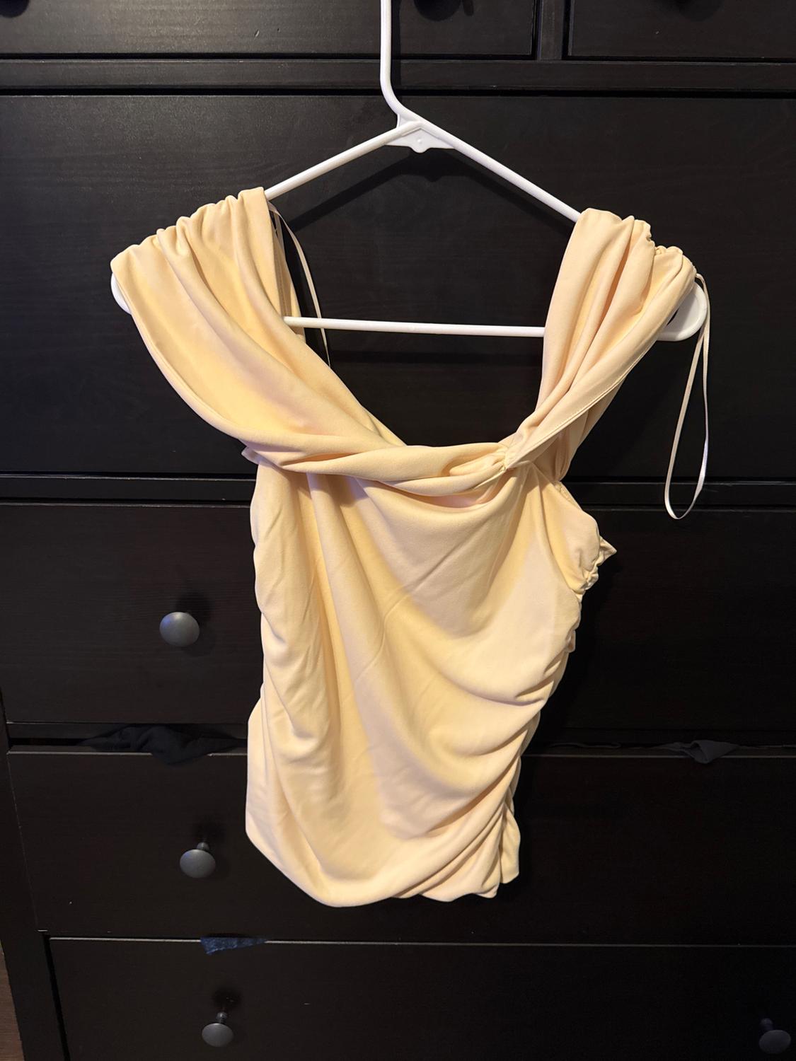 Draped yellow top hanging on a white hanger in front of a dark cabinet with drawers.