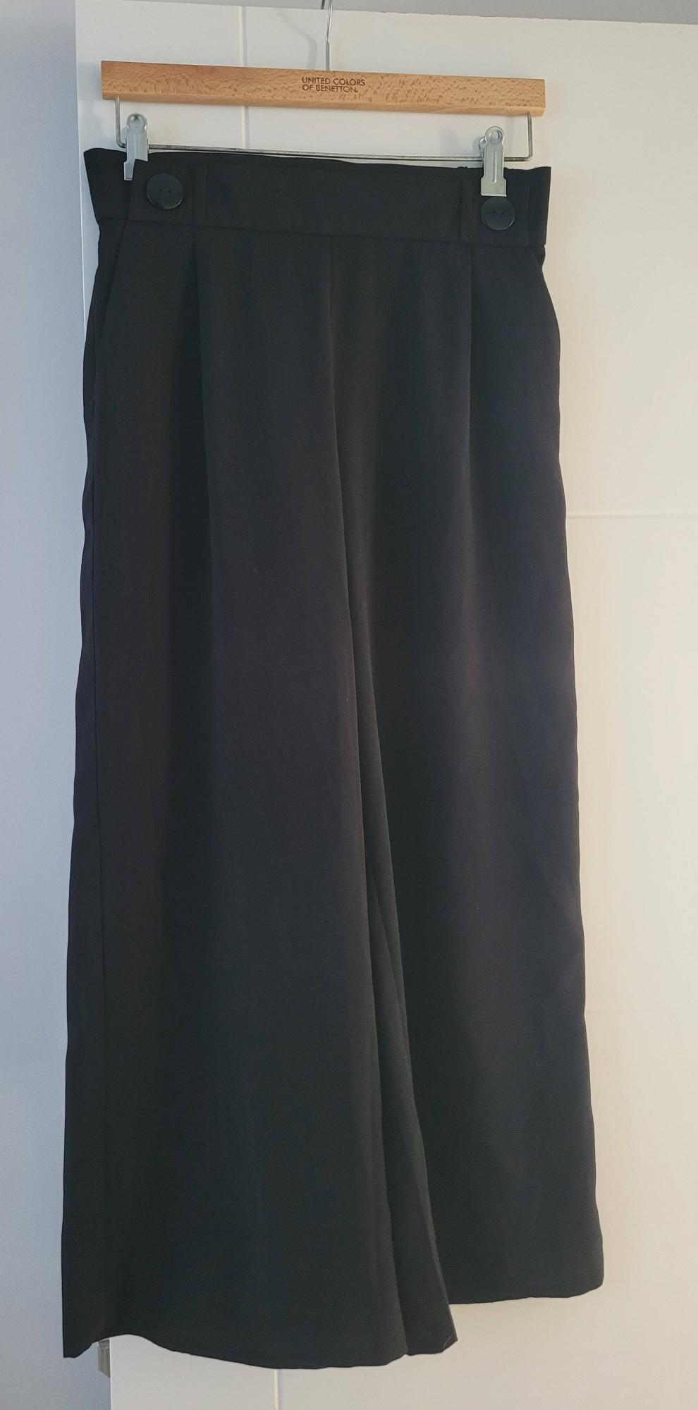 Black trousers hanging on a wooden hanger with the "United Colors of Benetton" brand engraved. White background.