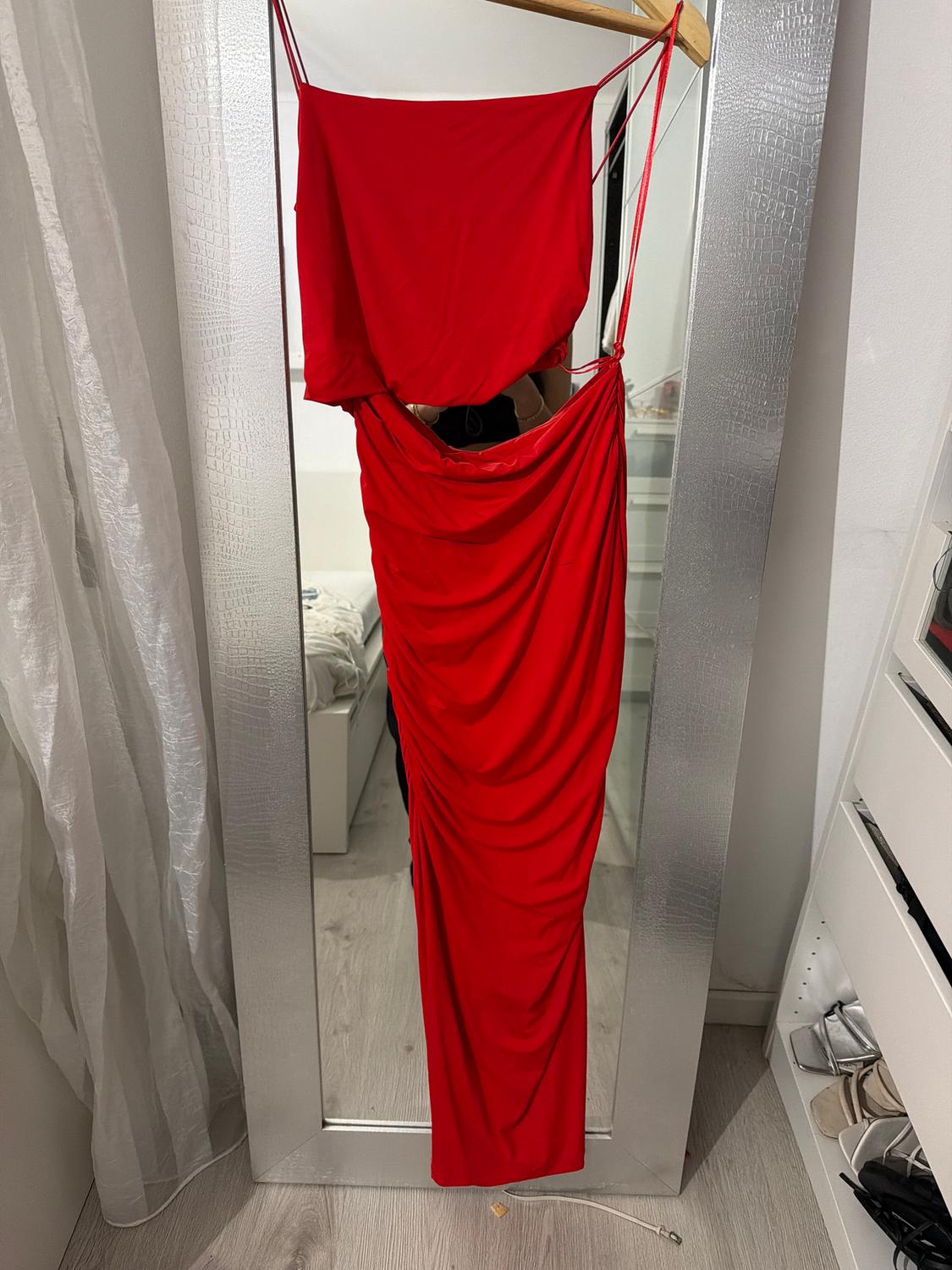 Red draped dress hanging on a full-length mirror, with a white room and sheer curtains in the background.