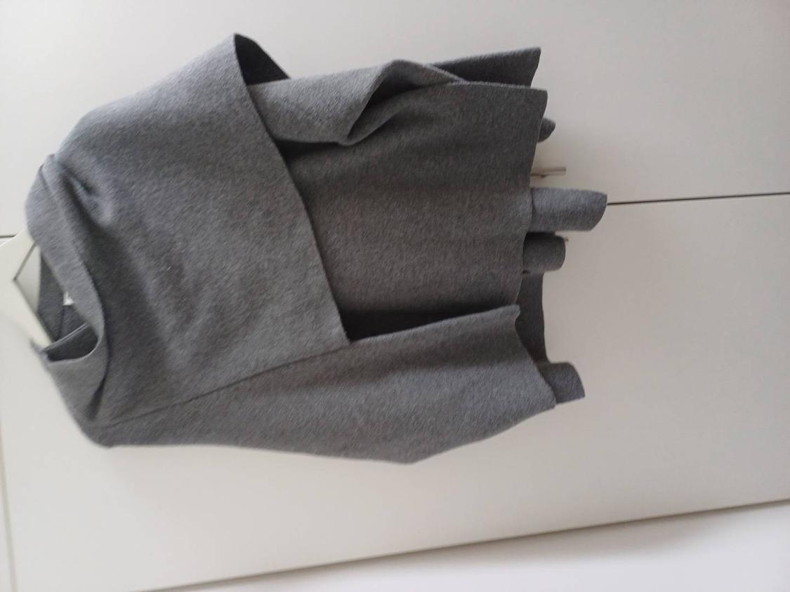 Grey wool jacket hanging on a white hanger against a white background. The garment has a modern, asymmetrical design.