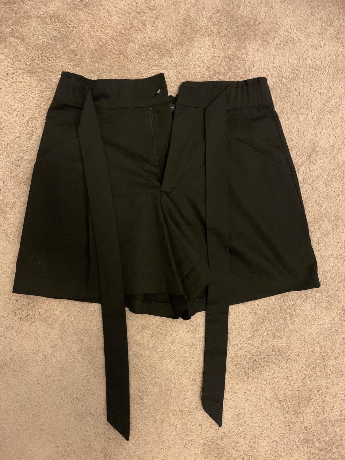 Black shorts with long waist ties, laid out on a beige rug.