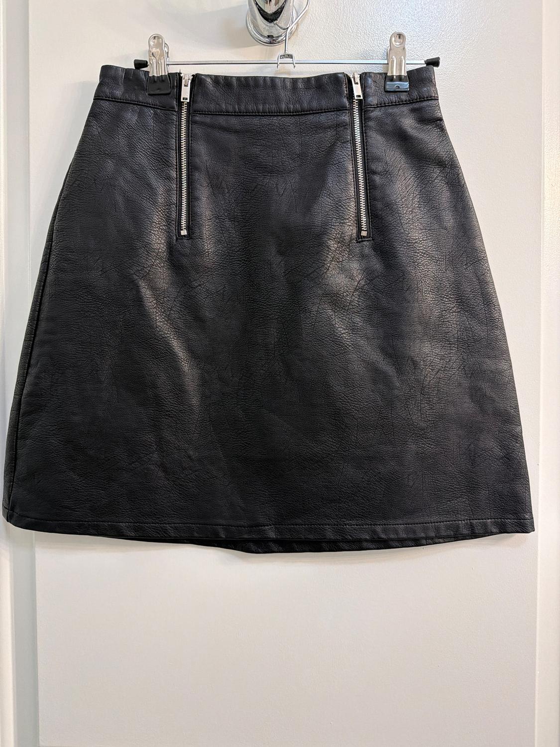 Black synthetic textured skirt with two vertical zippers on the front, hanging on a white hanger.
