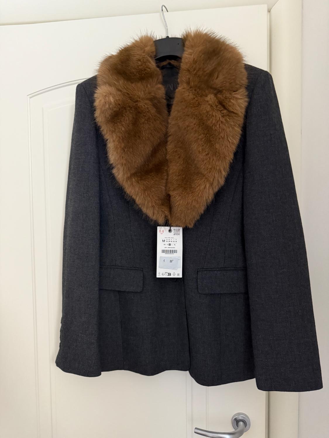 Grey jacket with a brown fur collar hanging on a white door. Visible tag with a price of 89 euros.