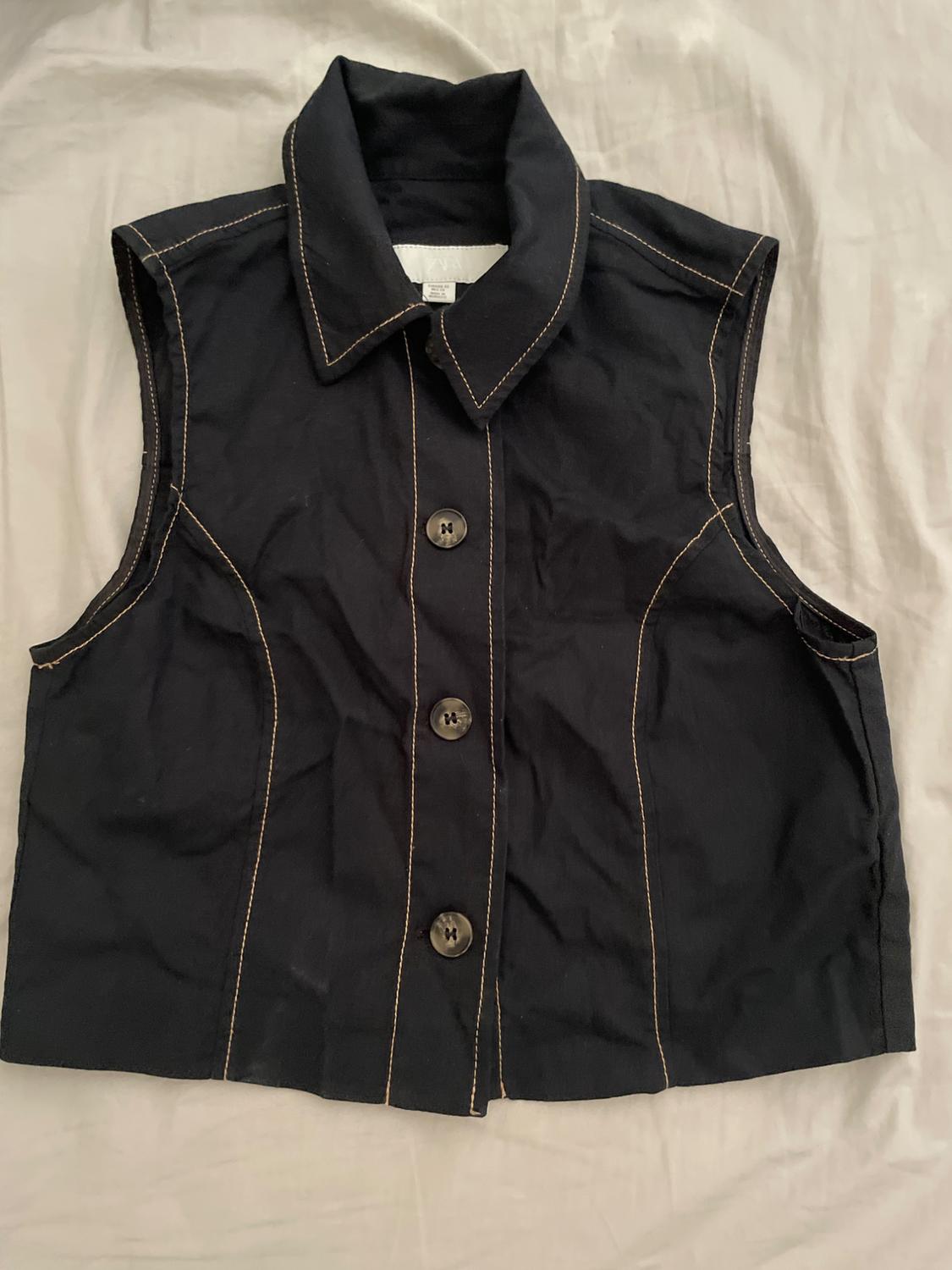 Black sleeveless waistcoat with visible stitching and front buttons on a light background.