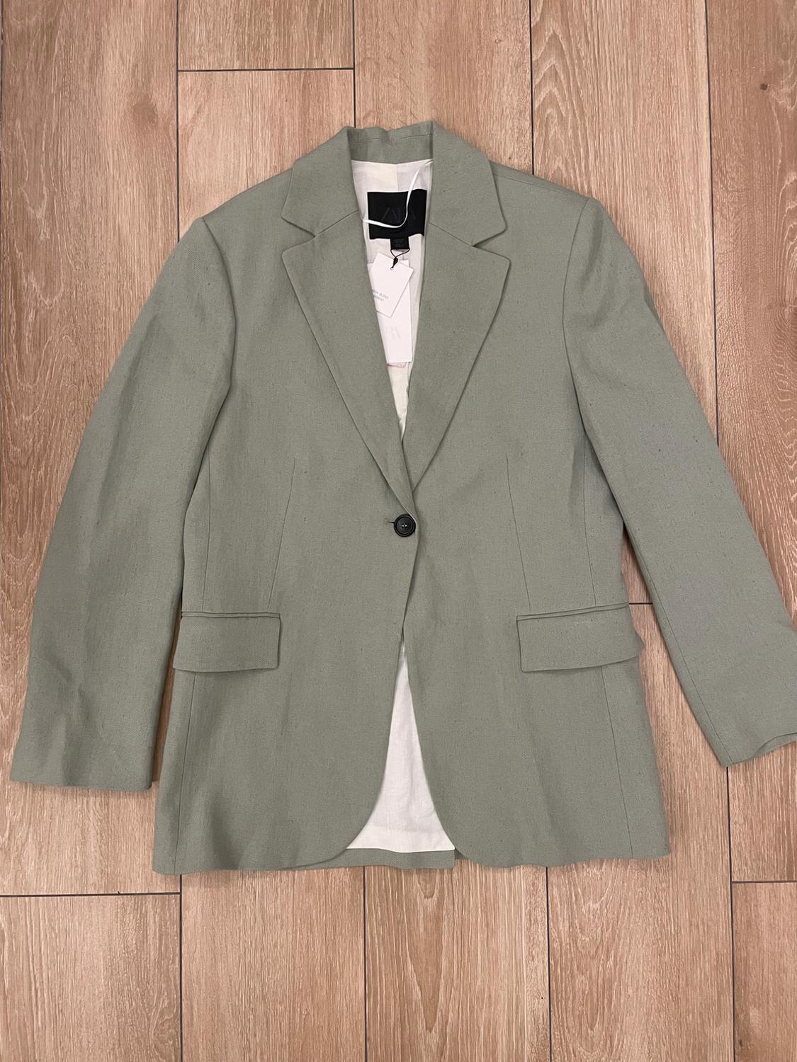 Light grey single-button jacket on a wooden floor. White label visible inside the collar.