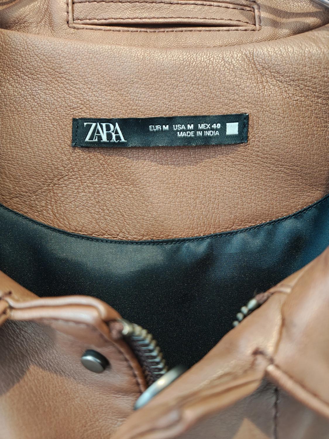 Brown jacket label with text: "ZARA EUR M USA M MEX 40 MADE IN INDIA". Visible zip and metal button detail.