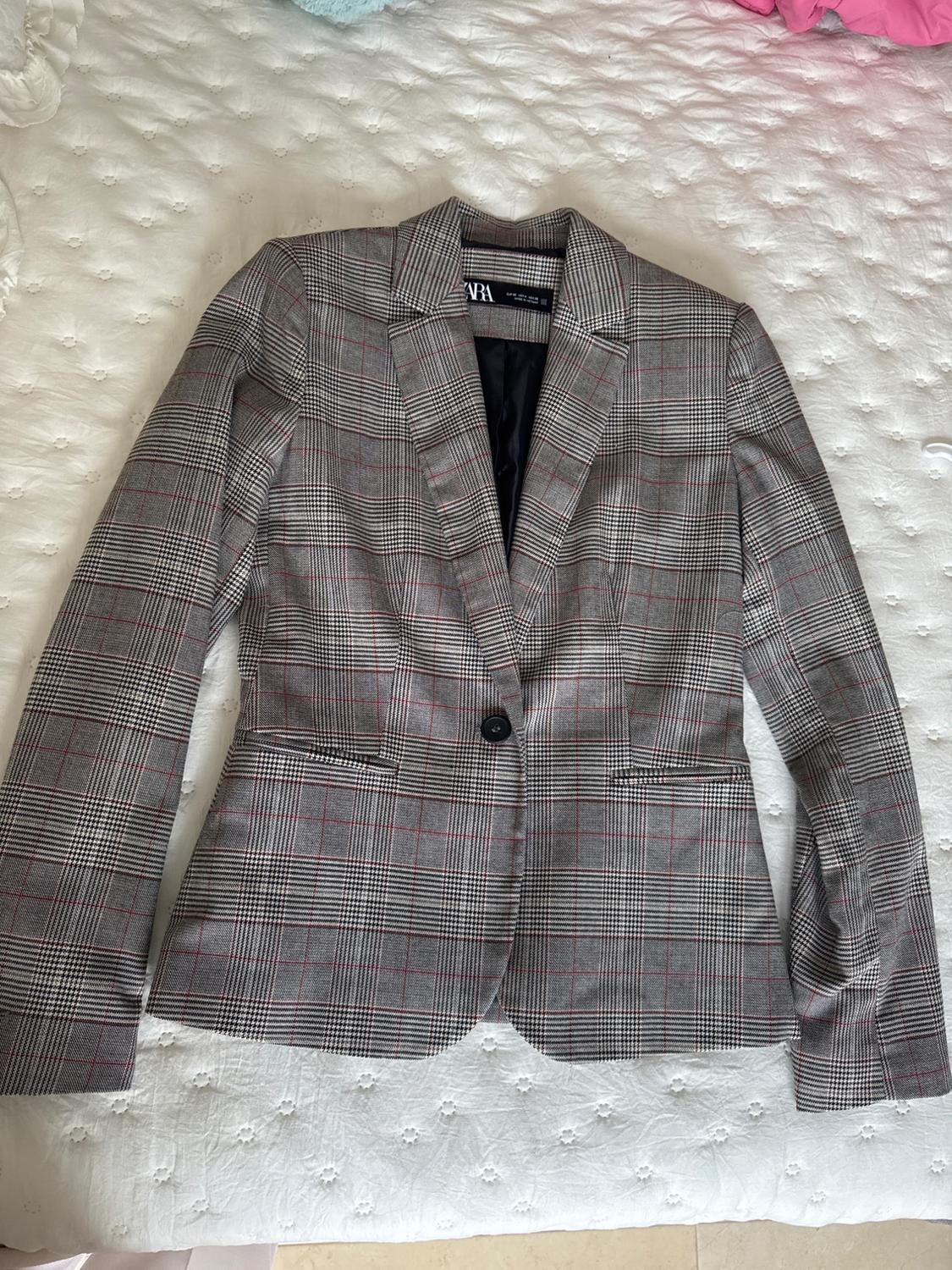 Grey checked blazer with red lines and a black button, on a white bedspread with a floral texture. Label visible inside.