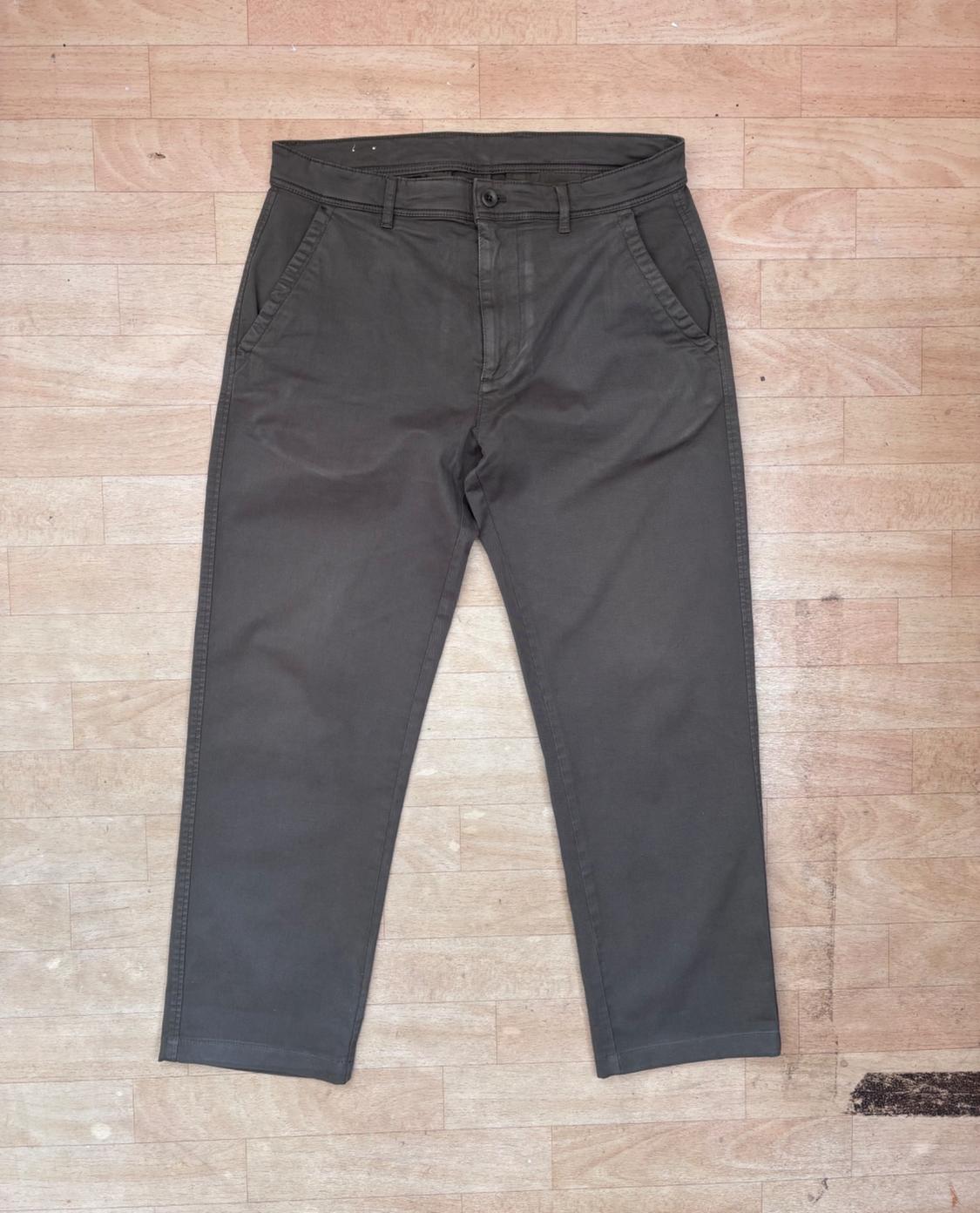 Dark grey casual trousers laid out on a light wood floor. Front view with side pockets and button fastening.