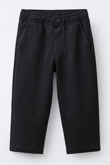 Front view of black pants with elastic waistband, front button, and side pockets.