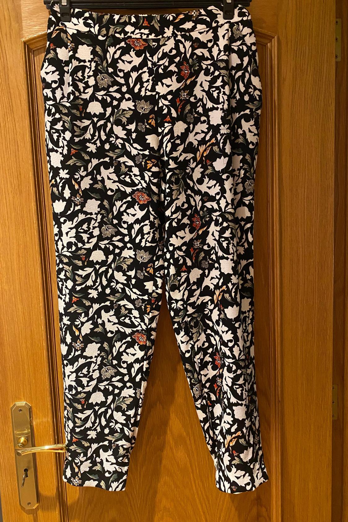 Front view of trousers with floral print in black, white and red, visible side pockets.