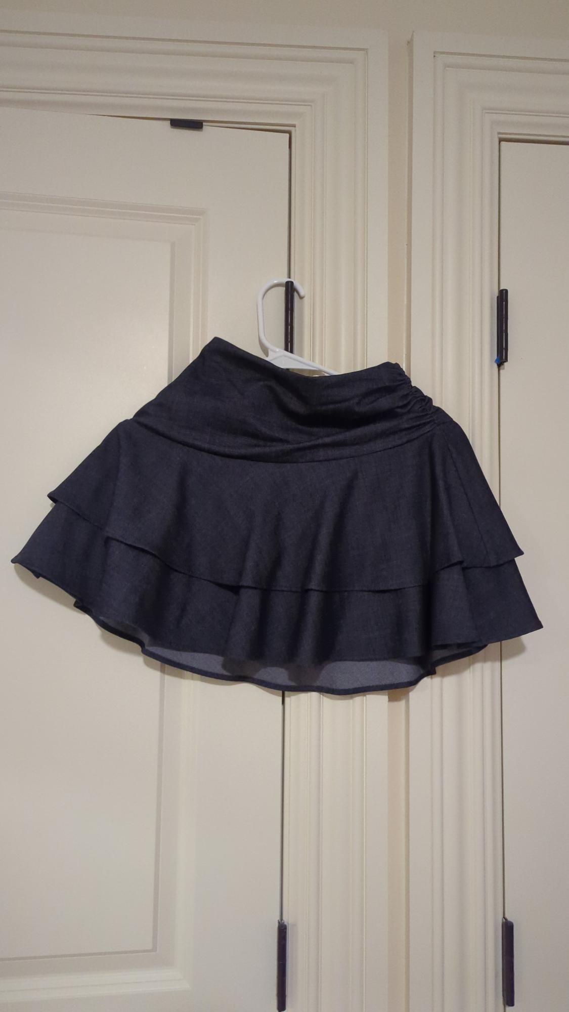 Black ruffled mini skirt hanging on a white hanger over a light wooden door.