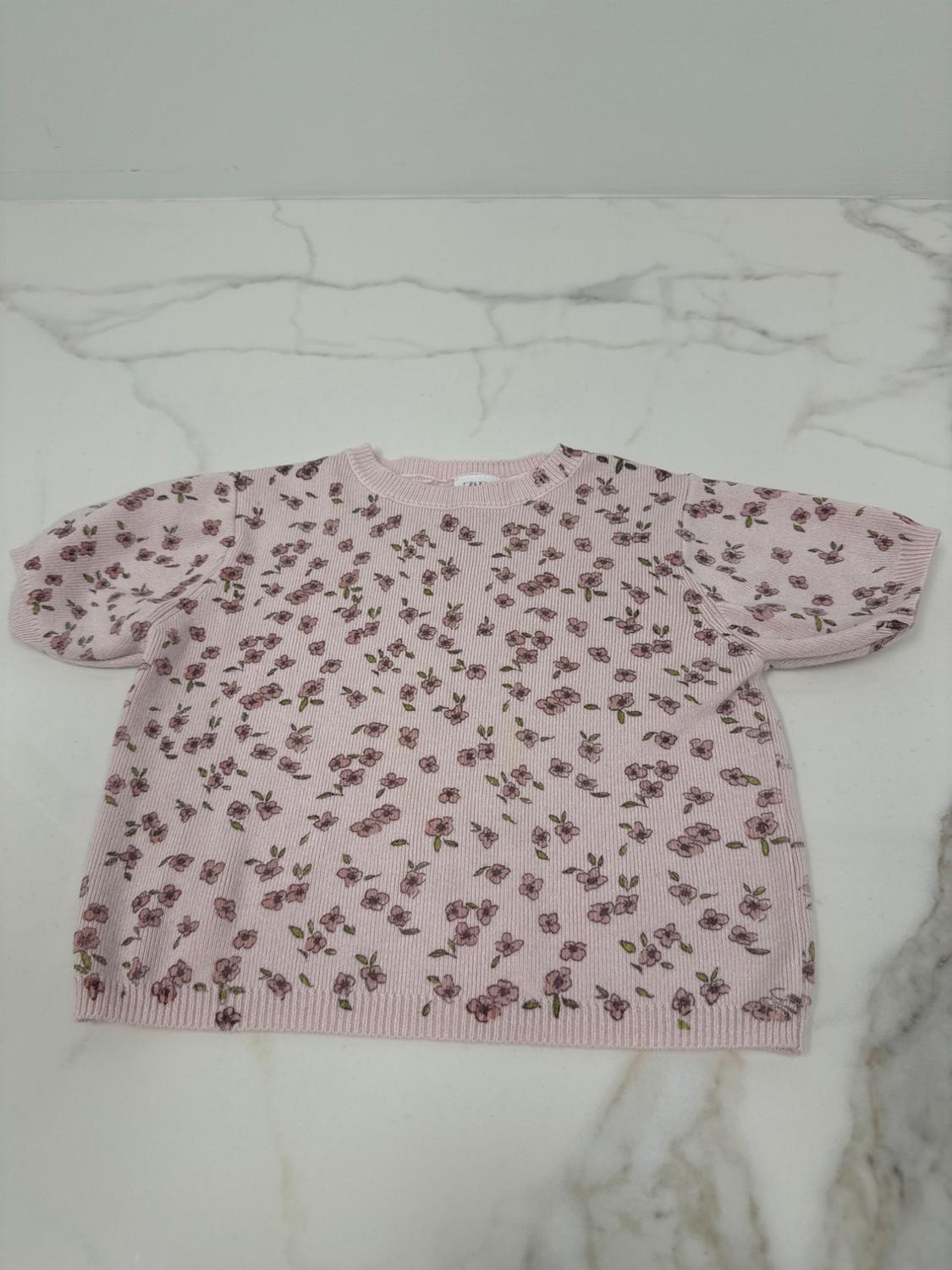 Light pink jumper with a small floral print in shades of pink and green, on a white marble surface.