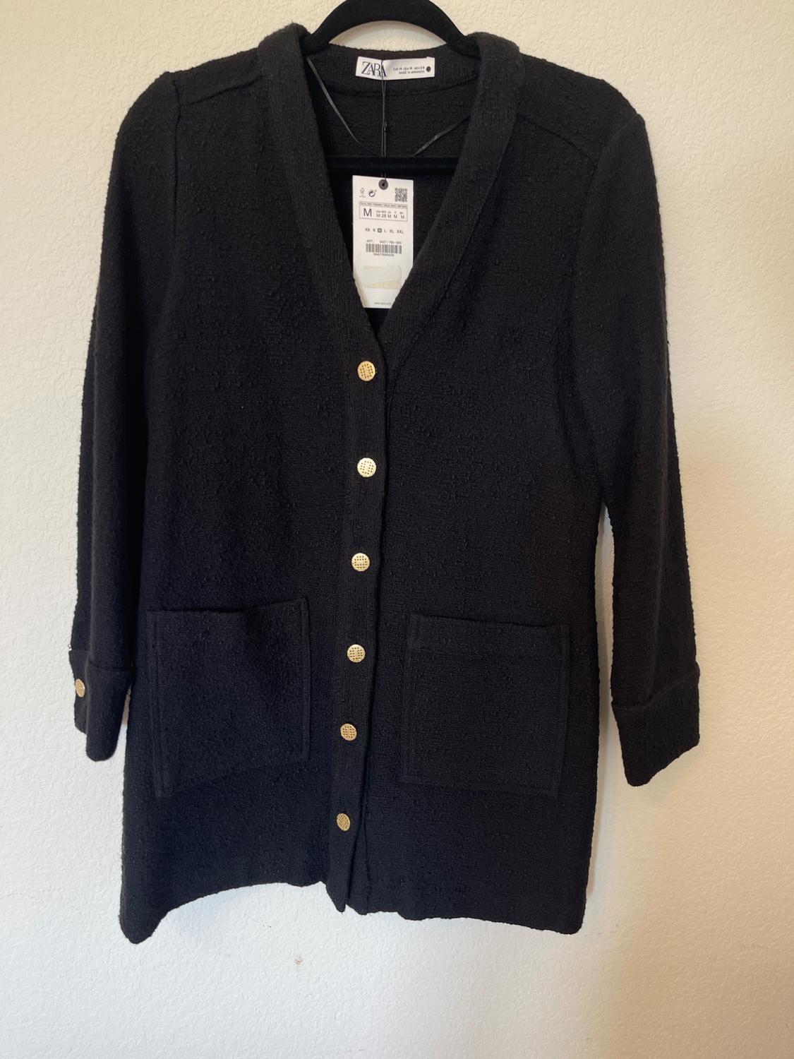 Black knitted jacket with gold buttons and two front pockets. Visible label with size and brand details.