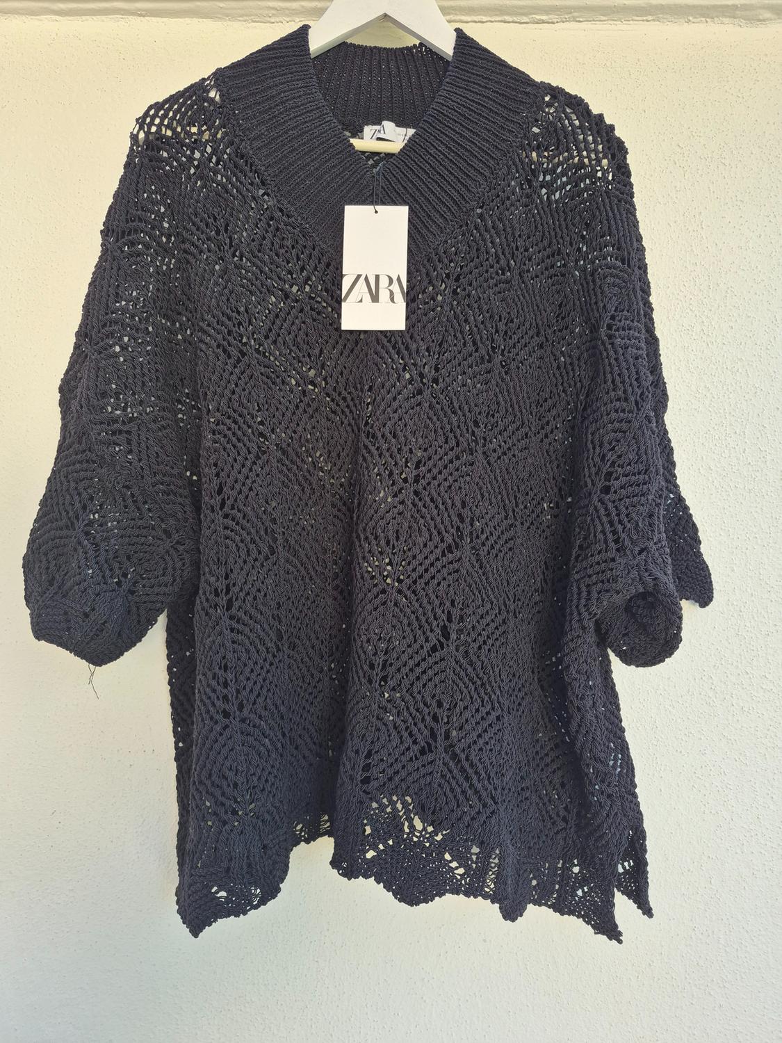 Black knitted jumper hanging on a white hanger, with the 'ZARA' brand label visible in the centre. White background.