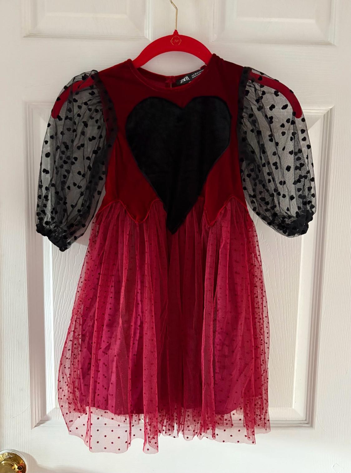Red Zara dress hanging on a white door. It features a black heart on the front, sheer black sleeves, and a red polka-dot tulle skirt.