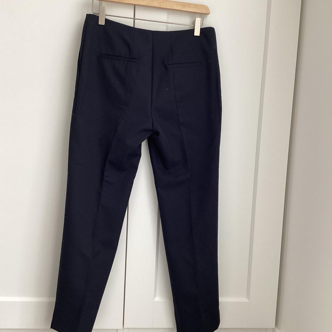 Black trousers hanging on a wooden hanger in front of a white door.