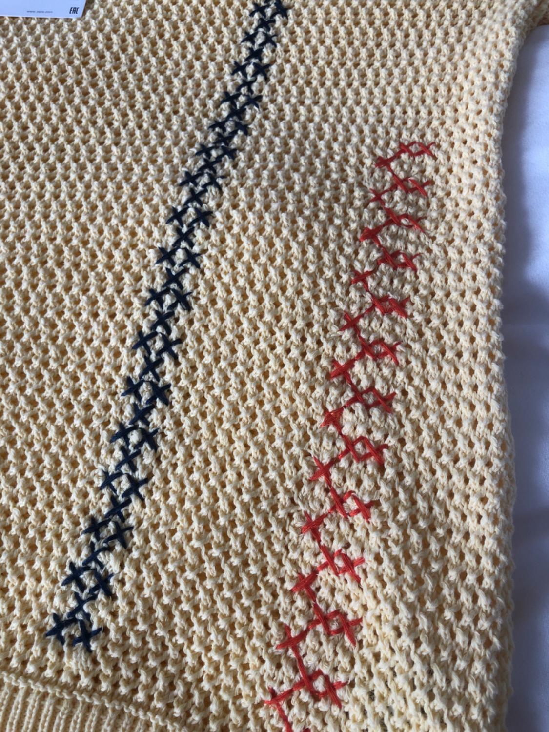 Beige knitted jumper with blue and red zigzag stitching details. Visible label in the top left corner.