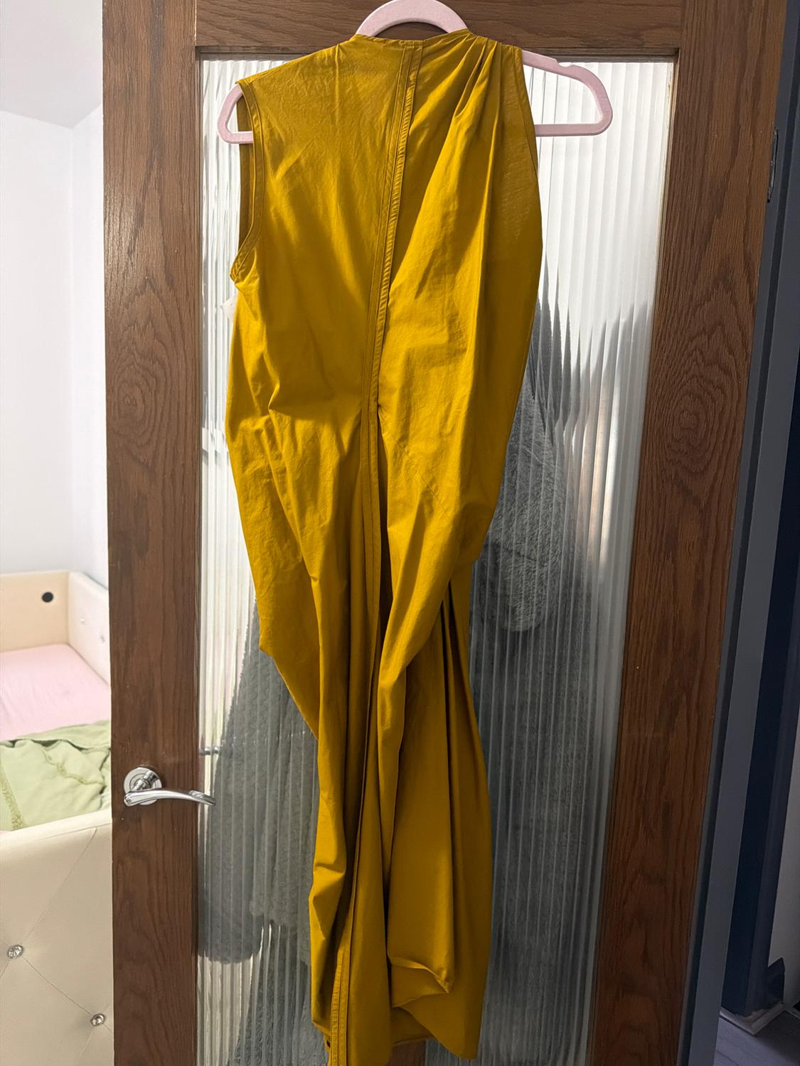 Yellow dress hanging on a wooden door with frosted glass. Room background with bed and green and pink bedding.
