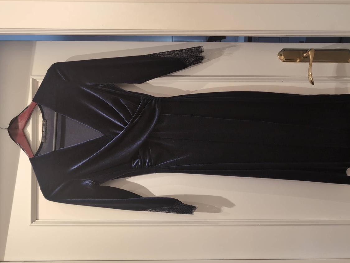 Dark velvet dress with a V-neckline, crossover waist, and lace cuffs, hanging on a hanger over a white door.