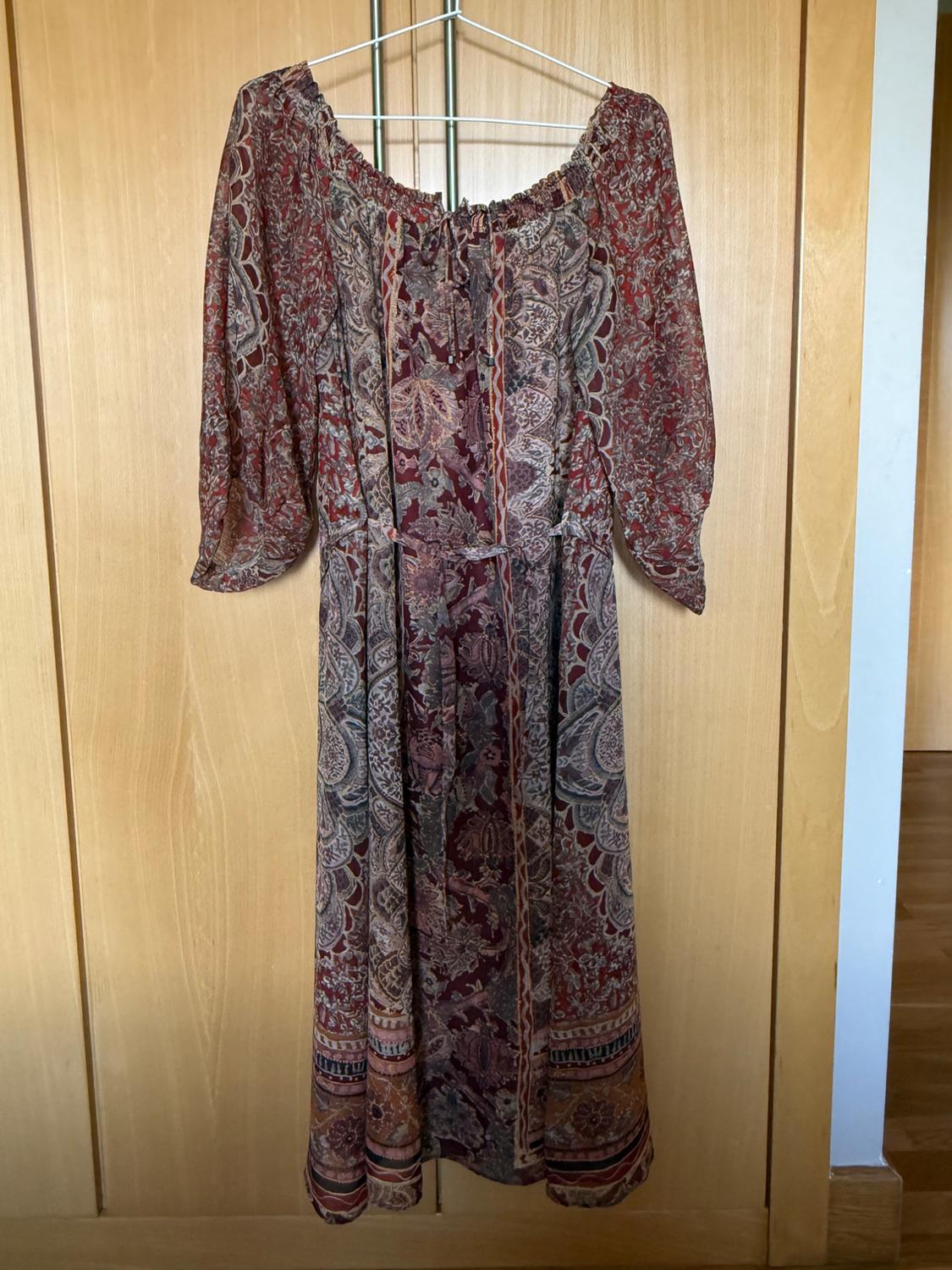 Front view of a long-sleeved, elasticated neckline printed dress in brown and red tones.