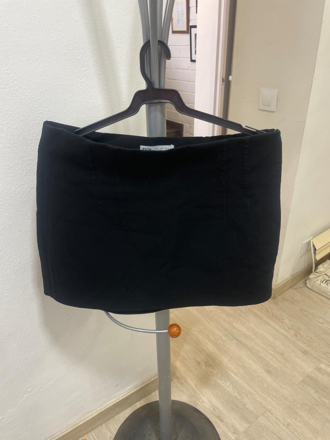 Black skirt hanging on a metal coat rack in a room with wooden floor and white walls. Label visible at the top.