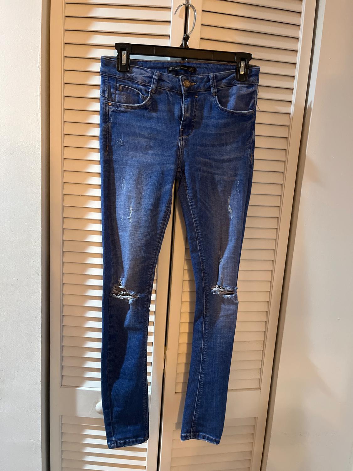 Worn blue jeans hanging on a black hanger in front of a white slatted door.