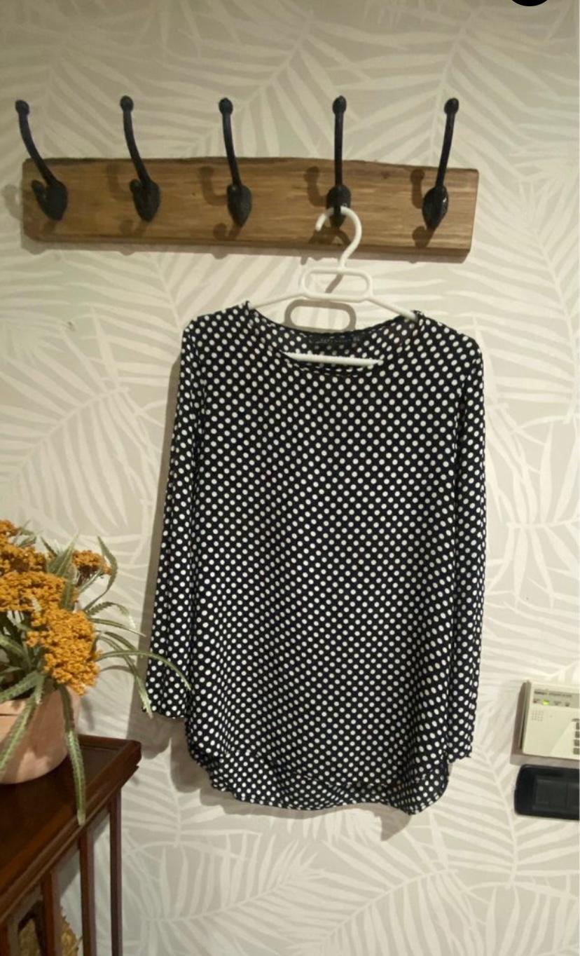 Front view of a white polka dot blouse on a black background with long sleeves.