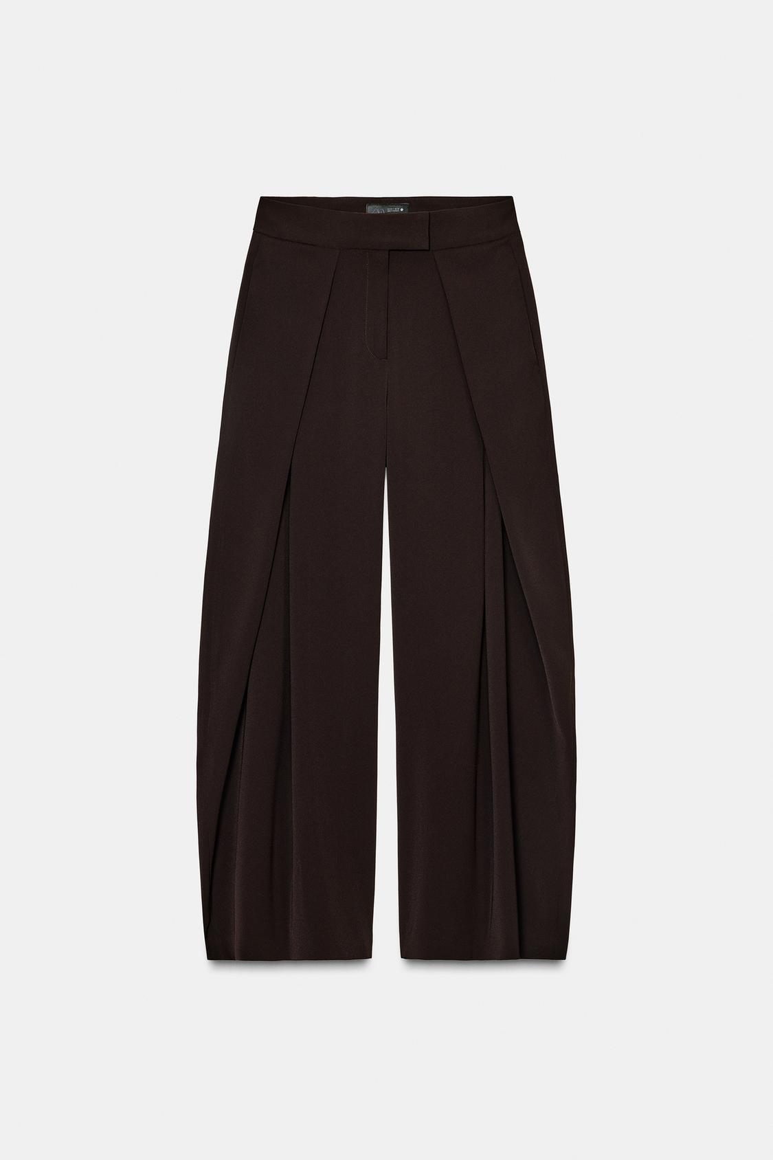 Front view of flowing brown trousers with pleats and concealed side pockets. Side zip fastening.